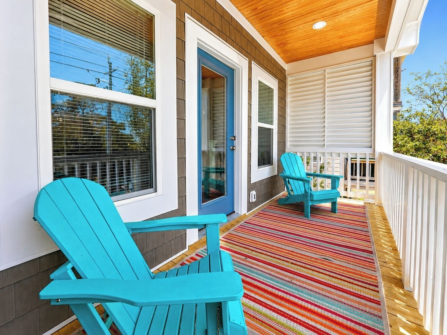 Eine überdachte Veranda mit zwei Adirondack-Stühlen, einem bunten Streifen Teppich und einer Holzbeschichtung.