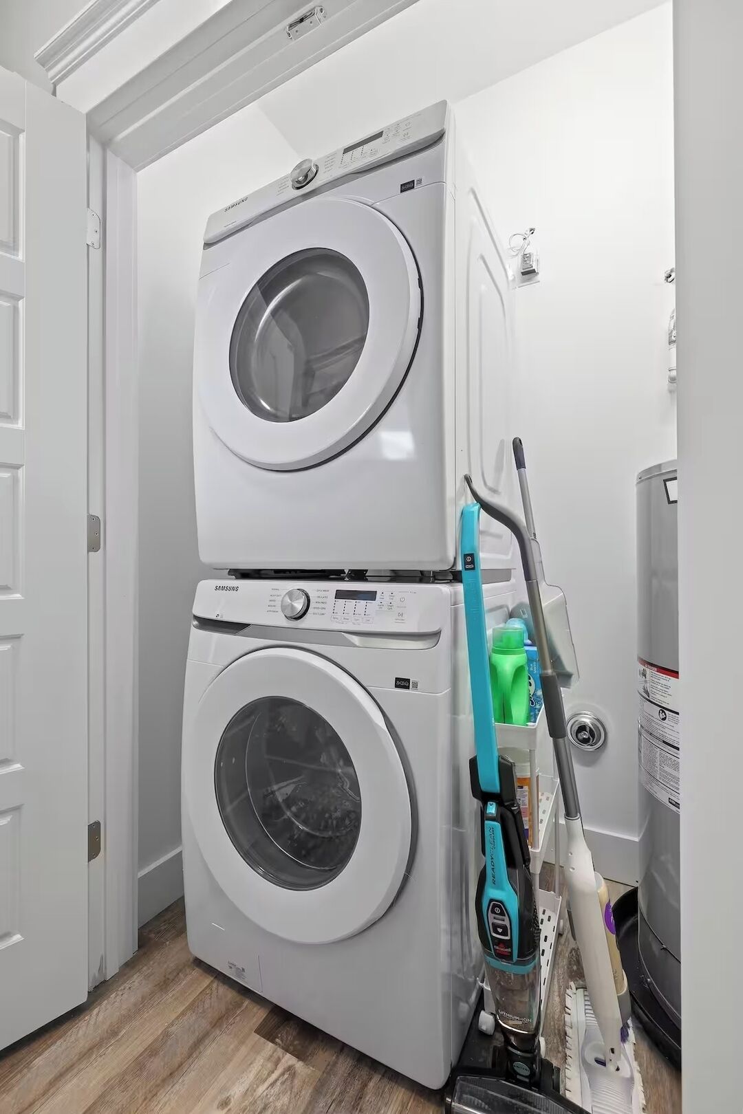 Una sala de lavandería con dos lavadoras apiladas, una herramienta para fregar y un calentador de agua.