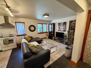 Un salon comprenant un canapé, un téléviseur, un coin cuisine et des éléments de décoration.