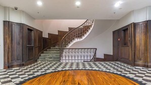 Una imponente escalera con barandales ornamentados, piso a cuadros y paneles de madera oscura.