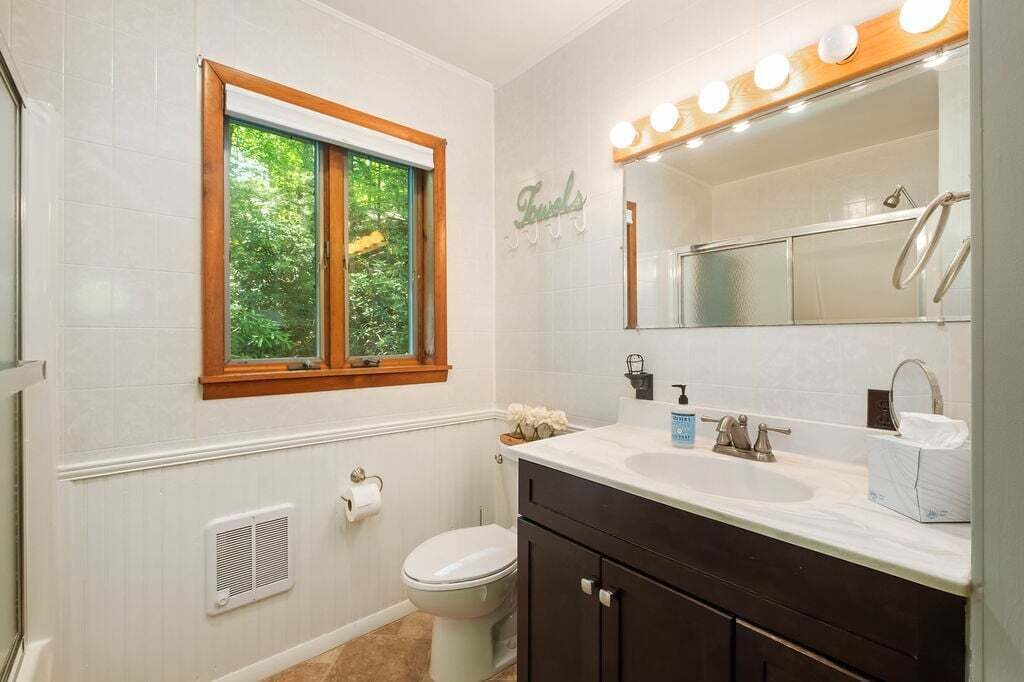 Une salle de bain avec une fenêtre, un lavabo, des toilettes et un meuble-lavabo avec un miroir.