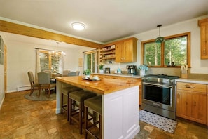 A kitchen with a central island, wooden cabinets, a built-in oven, and a window with a view of trees. - Spacious 7BR retreat with hot tub, fire pit, dock, and year-round views (Swanton)