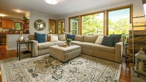 Un salon avec un canapé d’angle, un pouf et un tapis à motifs.