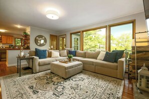 A living room with a sectional sofa, ottoman, and patterned rug. - Spacious 7BR retreat with hot tub, fire pit, dock, and year-round views (Swanton)