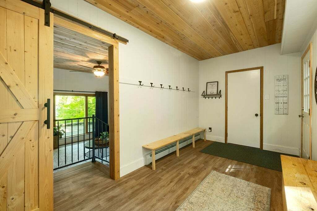 A room with wooden flooring, a bench, a door, and a wall-mounted coat rack.