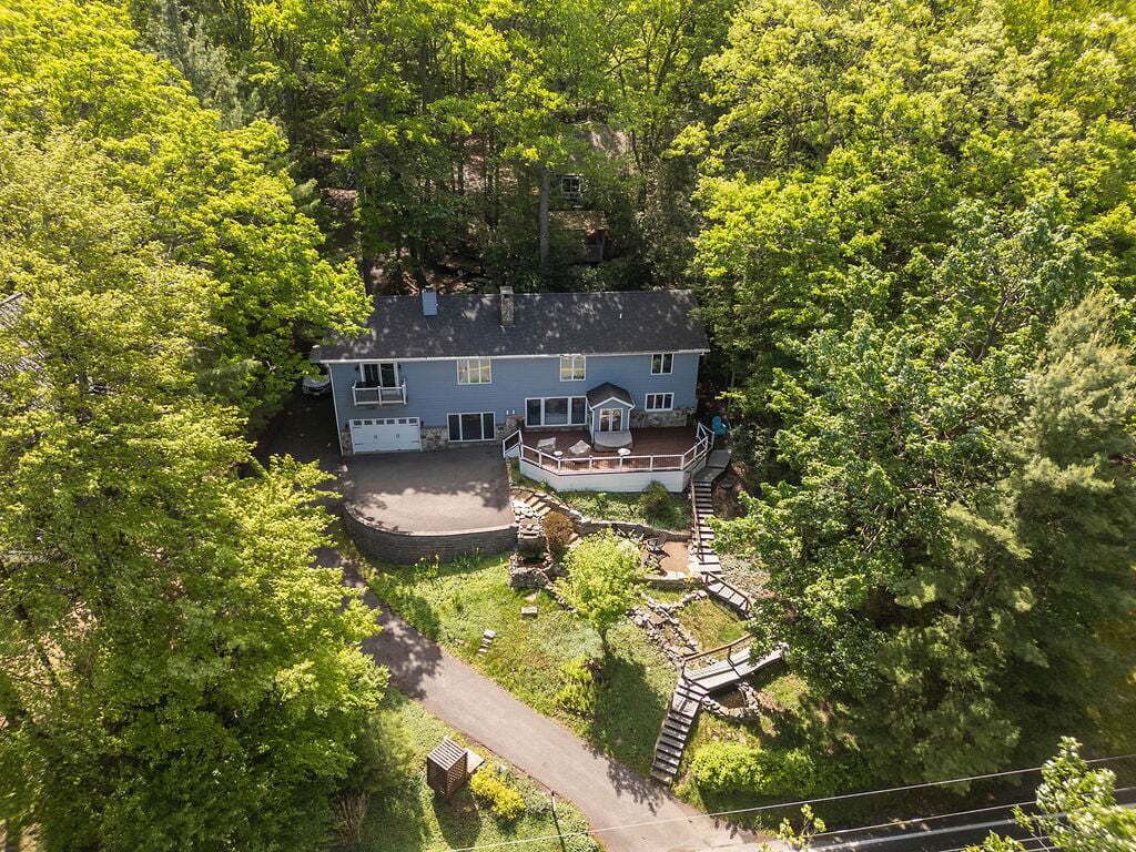 A two-story house with a porch, surrounded by dense trees.