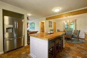A kitchen with a stainless steel refrigerator, wooden island, and bar stools. - Spacious 7BR retreat with hot tub, fire pit, dock, and year-round views (Swanton)