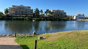 A waterfront hotel with multiple balconies, a grassy area, and a body of water. - Pacifika Mazatlan Studio (Mazatlán)