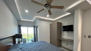 A hotel room with a bed, a ceiling fan, a TV, and a view of the outdoors. - Pacifika Mazatlan Studio (Mazatlán)