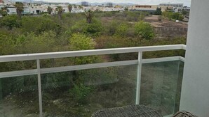 A balcony with a wicker chair and a table, overlooking a residential area with buildings and greenery. - Pacifika Mazatlan Studio (Mazatlán)