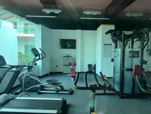 Ein Fitnessraum mit Cardiogeräten, Gewichten und einem Fernseher an der Wand.