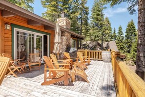 Une terrasse en bois avec des fauteuils Adirondack, une cheminée en pierre et une porte vitrée donnant sur un espace abrité.