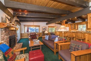 Interior acogedor de una cabaña con chimenea, muebles de madera y vistas al exterior.