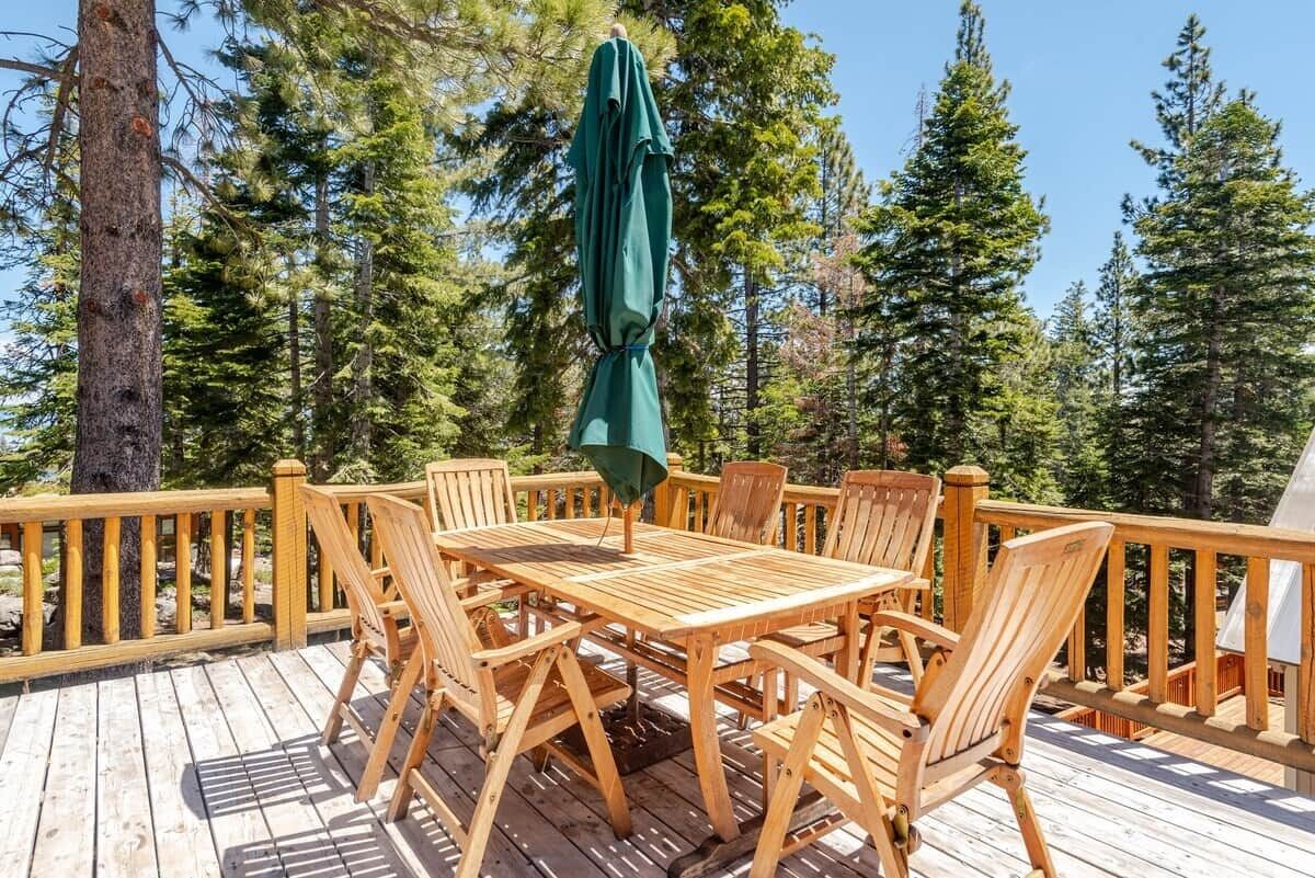 Eine Holzterrasse mit Tisch und Stühlen, umgeben von Bäumen.