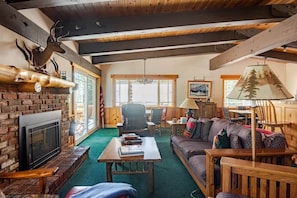 A cozy lodge interior with a fireplace, wooden furniture, and a large window. - Tahoe Group Oasis | 5BR, EV Charger & Fast Wifi (Tahoma)