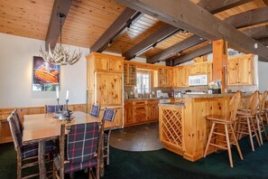 Une cuisine rustique avec des meubles en bois, une table à manger entourée de chaises à carreaux et un lustre.