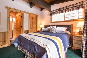 Un dormitorio con una cama grande, puertas de madera, una ventana con cortinas y una mesita de noche con lámpara.