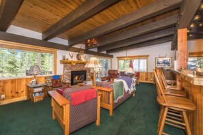 Un interior de cabaña acogedor, con chimenea, muebles de madera y ventanas grandes.