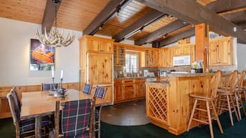 Une cuisine rustique avec des meubles en bois, une table à manger entourée de chaises à carreaux et un lustre.