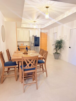 A modern kitchen with white cabinets, a black refrigerator, and a wooden dining table with blue cushioned chairs. - Spacious 2 bedroom apartment in charming Kingston with pool. (Kingston)