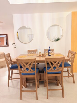A dining area with a round table, six wooden chairs with blue cushions, two wall-mounted mirrors, and a bottle on the table. - Spacious 2 bedroom apartment in charming Kingston with pool. (Kingston)
