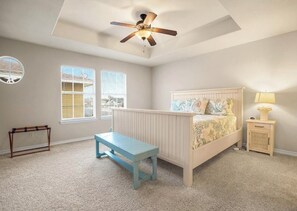 Ein Schlafzimmer mit einem Bett, einer Bank, einem Nachttisch, einem Deckenventilator und zwei Fenstern.