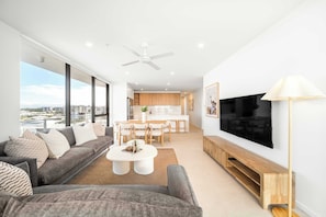 Ein modernes Wohnzimmer mit Sofa, Couchtisch, Fernseher und Blick auf die Stadt.