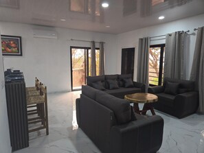 Un salon moderne avec un canapĂ© dâangle, une table basse en bois et un coin repas oĂč les assiettes sont empilĂ©es.