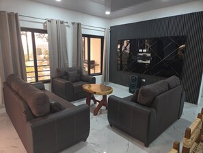 A modern living room with a sofa set, a wooden coffee table, and a large TV mounted on a wall.