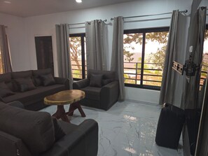 Uma sala de estar moderna com sofá em formato de L, uma mesa de centro redonda e janelas amplas com cortinas.