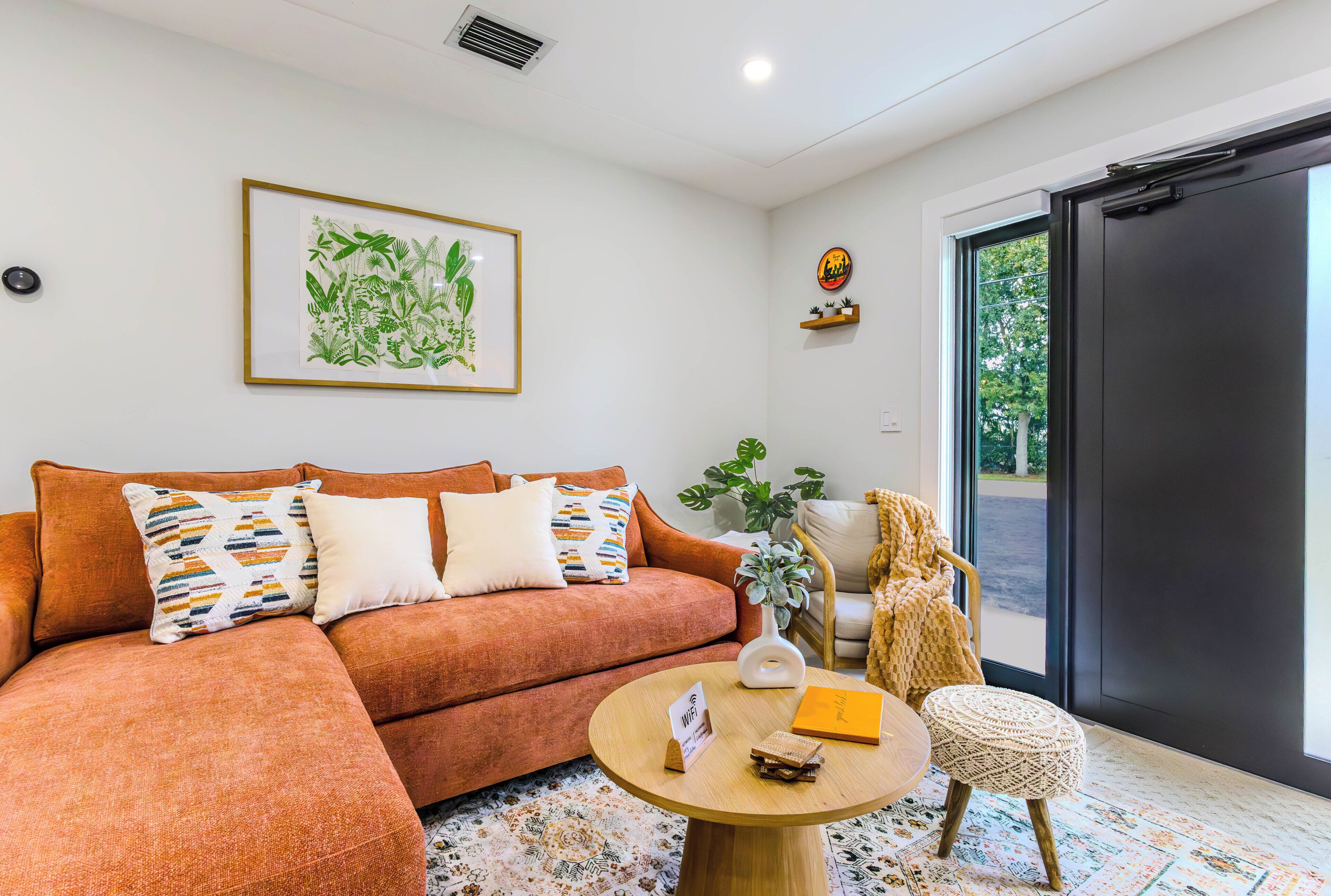 A living room with a sofa, a coffee table, a chair, a framed botanical print, and a window with a view.