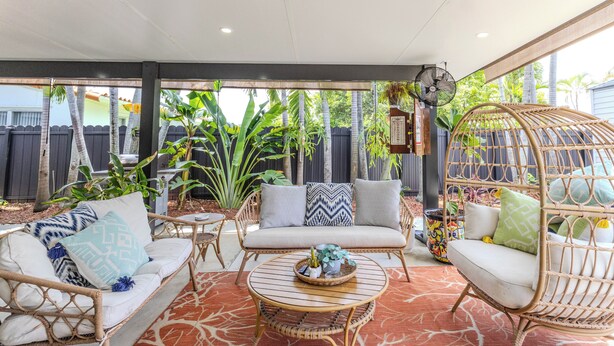 Une terrasse couverte, aménagée avec des meubles en osier, une table ronde et un fauteuil suspendu.
