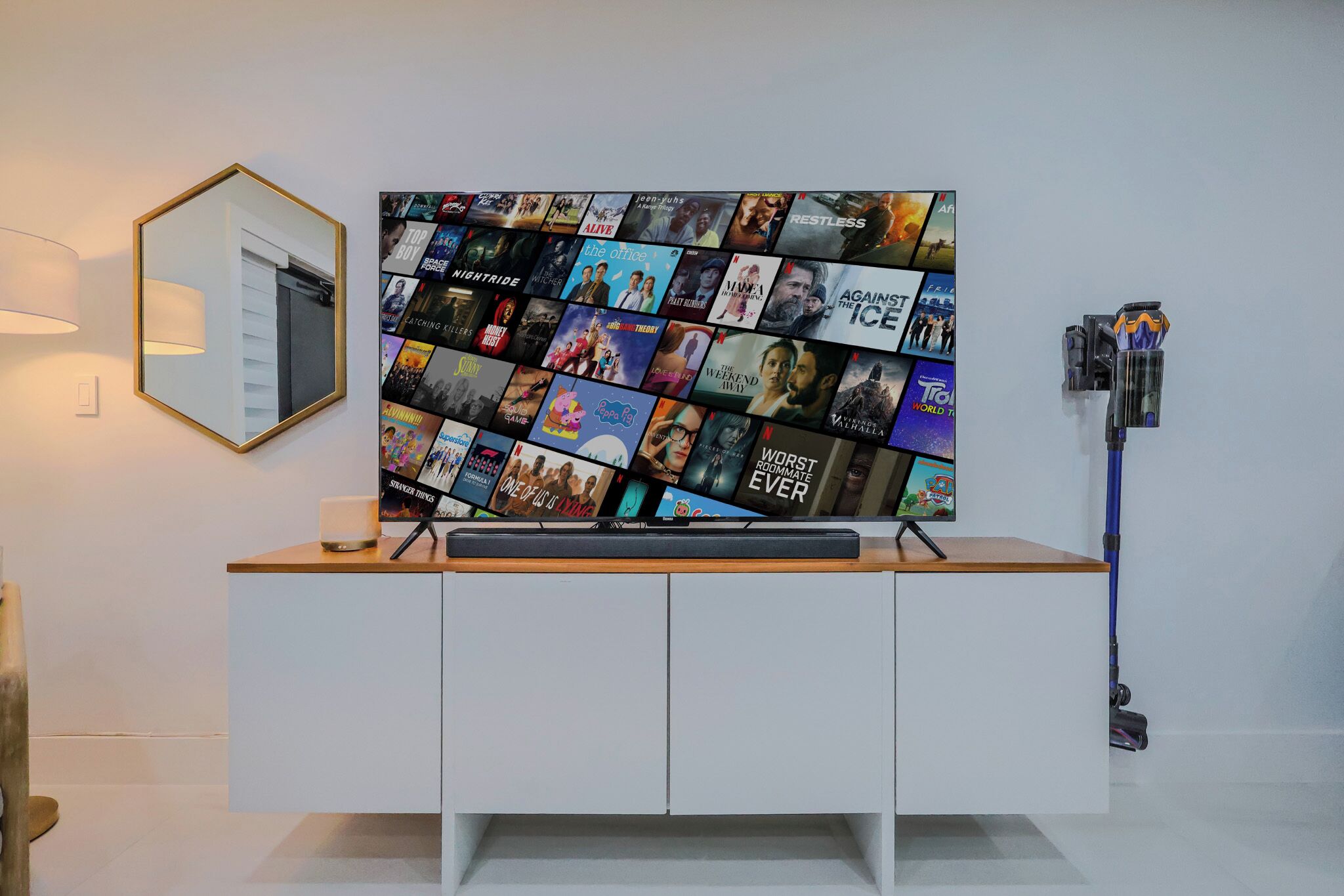 Un televisor de pared mostrando carteles de películas, un espejo y una aspiradora.