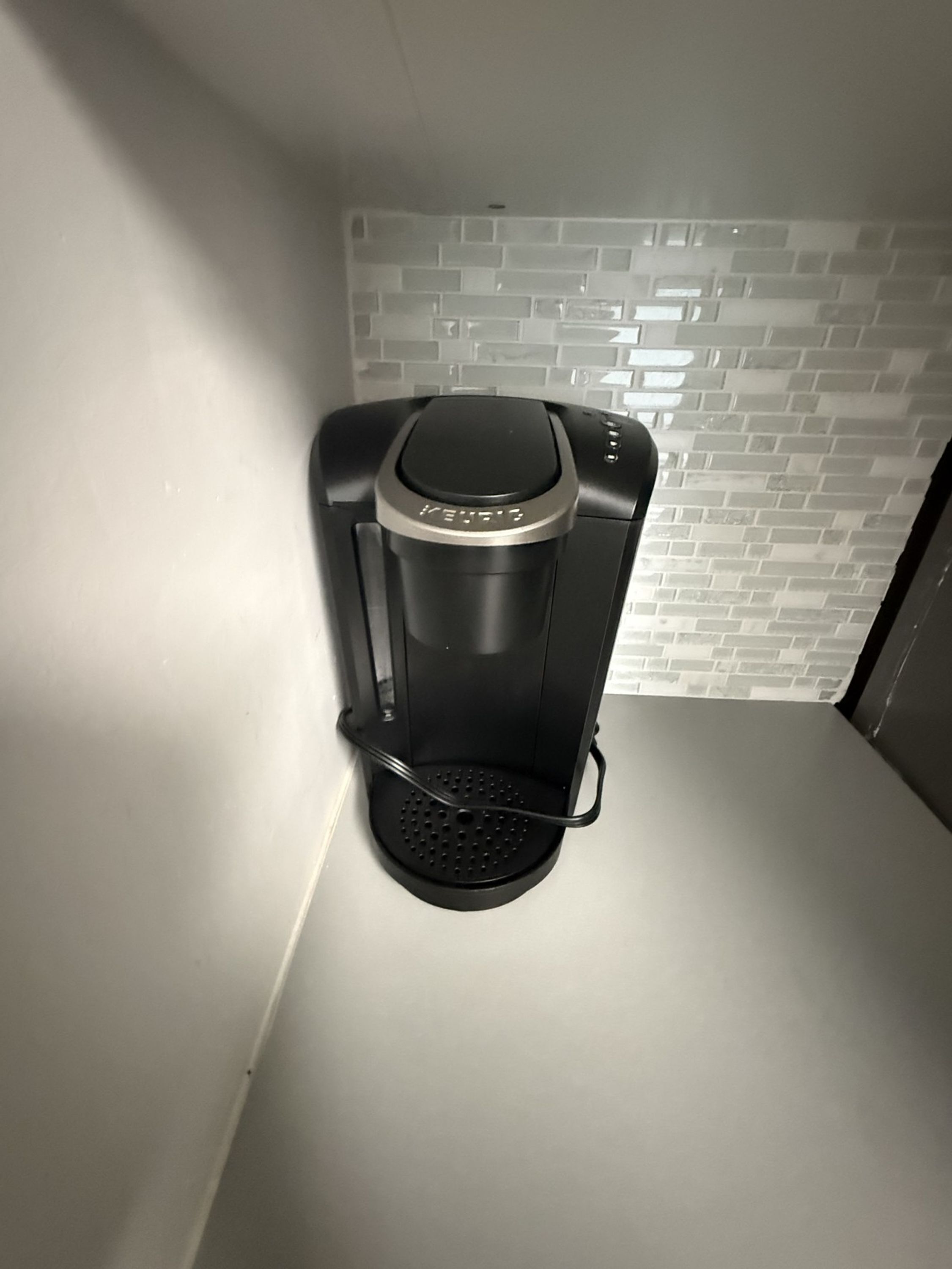 Una cafetera sobre una encimera con un revoque blanco de azulejos.