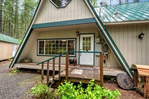 Eine Holzhütte mit Satteldach, einer Veranda mit Bank und einer kleinen Haustür.