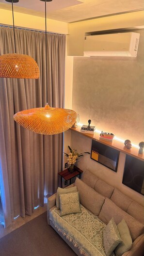 Ein modernes Wohnzimmer mit einer Couch, dekorativen Lampen, einem kleinen Tisch mit Büchern und einer Wand-Klimaanlage.