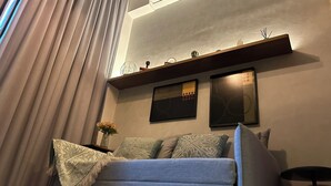 Un salón con un sofá, una mesita de noche con un jarrón y dos obras de arte colgadas en la pared.