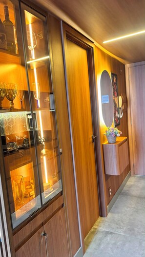 A hotel room with a wooden cabinet, a glass display case with wine glasses, a mirror, and a small table with a flower arrangement. - Novíssimo Studio Duplex no Ibirapuera.
Predio com piscina, academia e sauna (São Paulo)