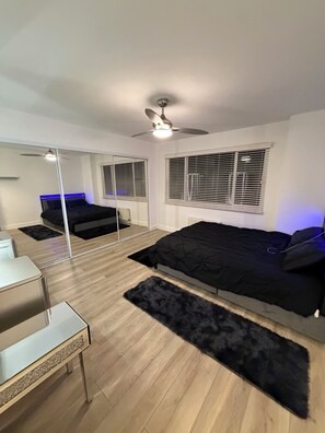 Ein Schlafzimmer mit Bett, Schreibtisch, Spiegel und Deckenventilator.