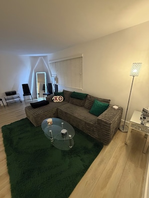 Ein stilvolles Wohnzimmer mit einem Ecksofa, einem Glastisch, einem grünen Teppich und einer Stehlampe.