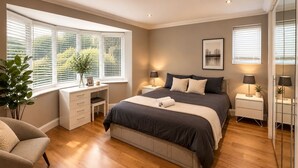 A bedroom with a bed, bedside tables, a desk, a chair, and large windows.