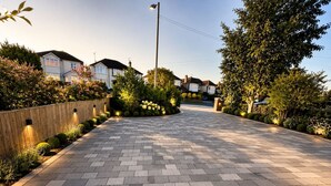 A paved driveway leading to a row of houses with a wooden fence and landscaped gardens.
