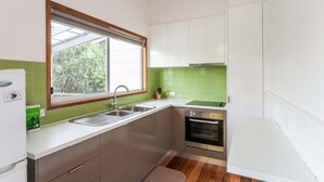 A compact kitchen with a window, a sink, a stove, and cabinets. - Aireys Inlet Beach House (Aireys Inlet)