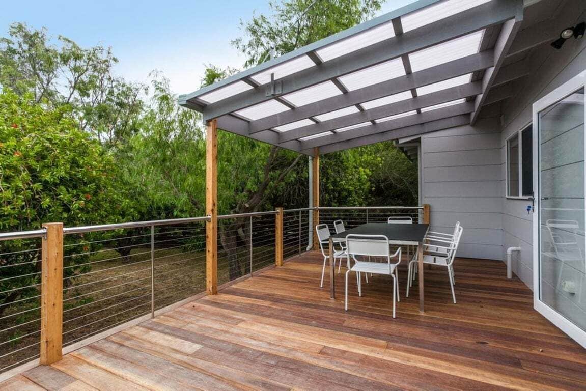 A covered outdoor patio with a table and chairs, surrounded by a wooden deck and metal railing.