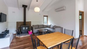 A modern living room with a fireplace, a sofa, a dining table, and a TV. - Aireys Inlet Beach House (Aireys Inlet)