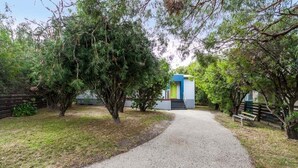 A gravel path leading to a building with a blue and white facade, surrounded by trees and a wooden fence. - Aireys Inlet Beach House (Aireys Inlet)