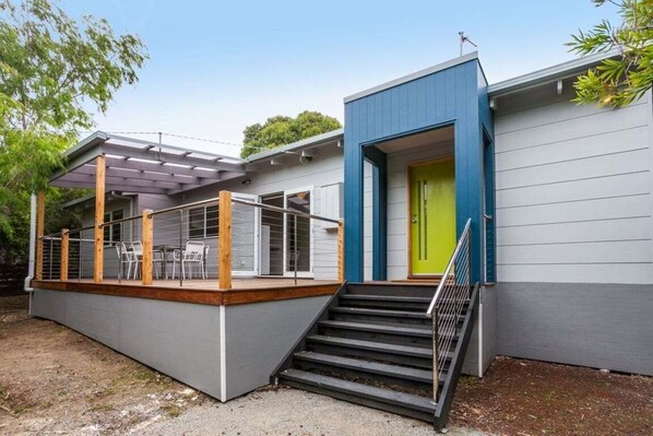 Una casa moderna amb un porxo cobert, una porta de color verd viu i una escala que condueix a l'entrada.