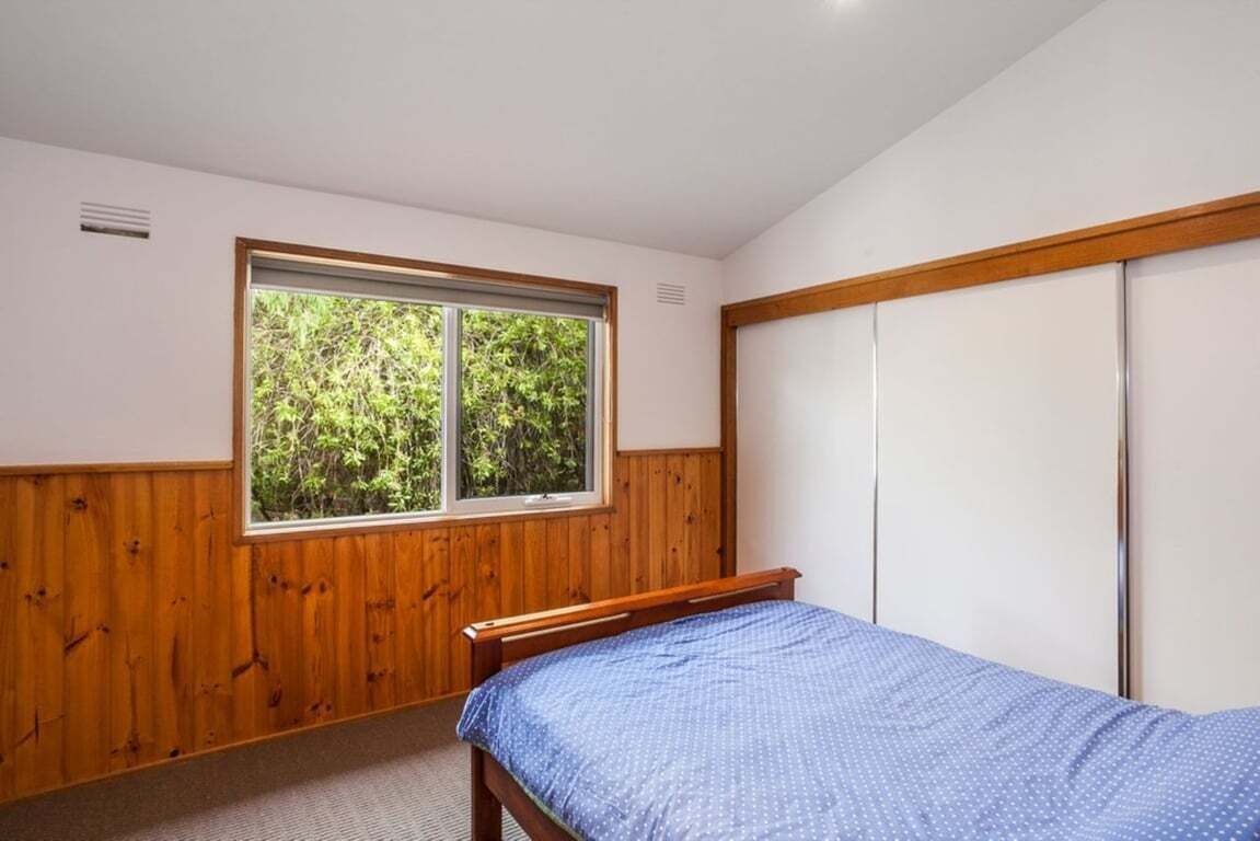 A bedroom with a single bed, a window with a view of greenery, and a wardrobe.
