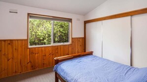 A bedroom with a single bed, a window with a view of greenery, and a wardrobe. - Aireys Inlet Beach House (Aireys Inlet)