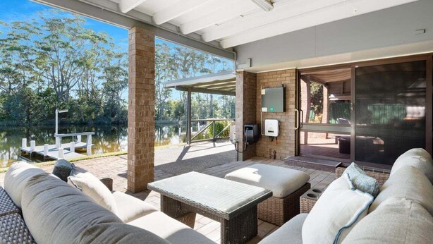 A covered outdoor seating area with wicker furniture, a brick wall, and a view of a lake. - Glassy Waters Sussex Inlet (Sussex Inlet)